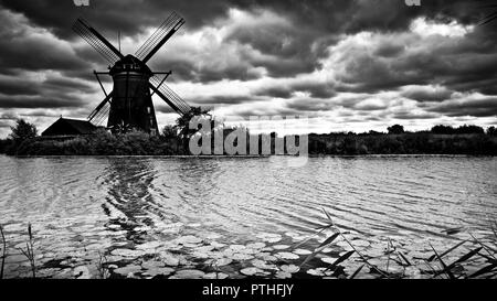 Künstlerische Darstellung in schwarz-weiß von traditionellen reetgedeckten holländischen Windmühle auf dem Kanalufer, gegen einen Sturm wolkigen Himmel, Kinderijk, Holland, Stockfoto