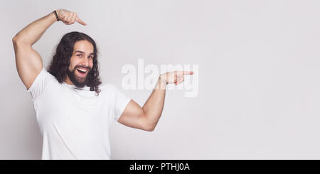 Portrait von starken Bodybuilder Mann im weißen T-shirt mit langen gewelltes Haar und Bart, stehend, mit Blick auf die Kamera mit toothy Lächeln und auf Licht Stockfoto