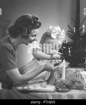 Weihnachten in den 1940er Jahren. Eine Mutter und ihre Tochter macht schöne Weihnachtsgeschenke. Sie fügen ein Wachssiegel auf der Verpackung, pehaps mit einem Stempel in Es sagen Frohe Weihnachten. Schweden 1940 Stockfoto