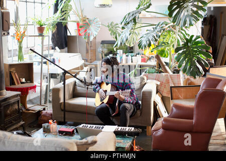 Junge männliche Musiker Aufnehmen von Musik, Gitarre spielen und singen Sie in das Mikrofon in der Wohnung Stockfoto