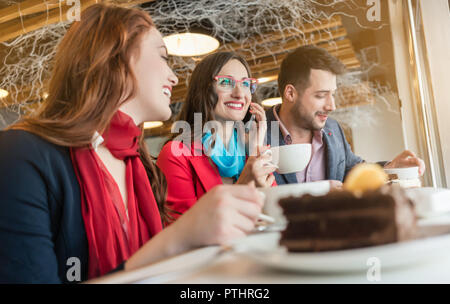 Low-Winkel auf eine trendige junge Frau, Gespräch am Handy und genießen Sie eine Tasse Kaffee mit Freunden oder Kollegen in einem modernen Cafeteria Stockfoto