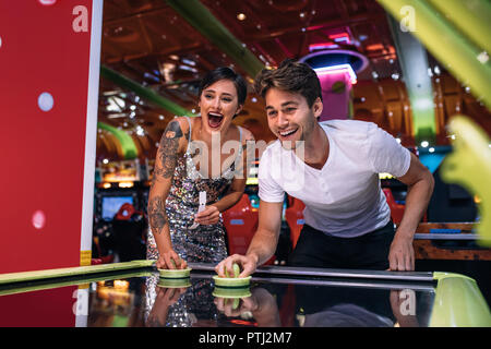 Paar spielen air hockey Spiel holding Stürmer in einem Spiel Salon. Aufgeregt, Mann und Frau Spaß Spiele spielen an einem Gaming Arcade. Stockfoto