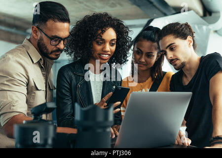 Fotograf mit seinem Team bei den Aufnahmen auf einem Laptop. Modell holding Handy mit Fotografen schießen Sie Fotos suchen. Stockfoto