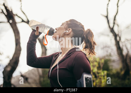 Frau trinkt Wasser nach einer Übung im Freien. Läuferin eine Pause und Trinkwasser aus der Flasche am Morgen. Stockfoto