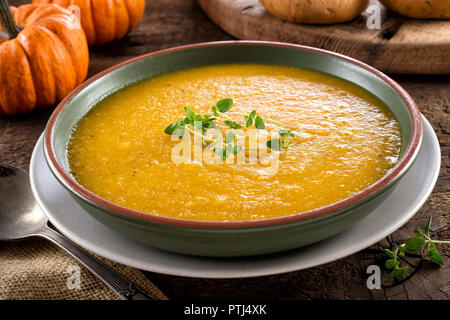 Eine Schüssel mit köstlichen hausgemachten Kürbis Kürbis Suppe mit frischem Thymian garnieren. Stockfoto