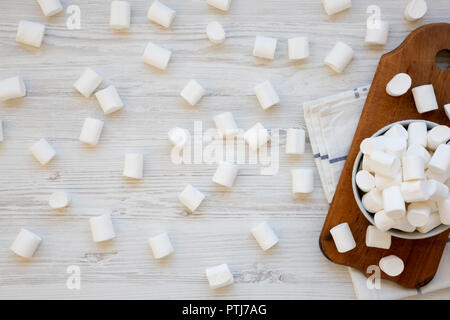 White Marshmallows in eine Schüssel auf rustikalen Holzbrett über weiß Holz- Hintergrund. Haufen flauschige Marshmallows. Ansicht von oben. Flach, von oben zu Stockfoto