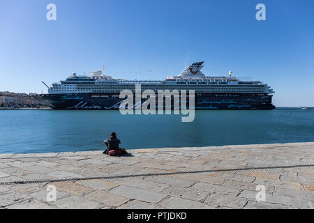 Frau sitzt auf der Audace Pier (Molo Audace) beobachtet ein luxuriöses Kreuzfahrtschiff Mein Schiff im Hafen von Triest angedockt, Friaul Julisch Venetien, Italien Stockfoto