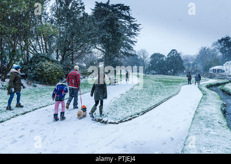 Eine Familie zu Fuß ihren Hund durch fallende Schnee in Trenance Gärten in Newquay in Cornwall. Stockfoto