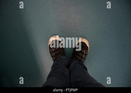 Blick hinunter auf ein Paar Beine und Schuhe stehen auf einem harten Boden. Stockfoto