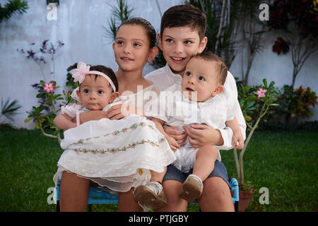 MERIDA, Yuc/MEXIKO - November 13, 2017: Bruder und Schwester halten Sie Ihr Baby twin Cousins vor der Taufe in der Kirche. Stockfoto