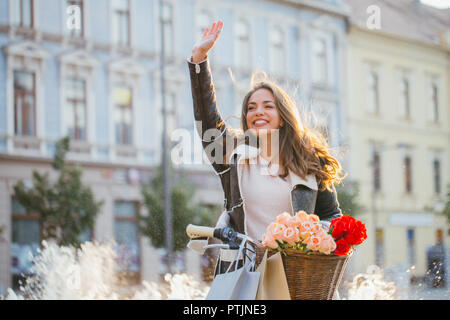 Schöne junge lächelnde Frau mit Fahrrad und winkende Hand auf Straße der Stadt. Schönheit, Geste und Lifestyle Konzept Stockfoto