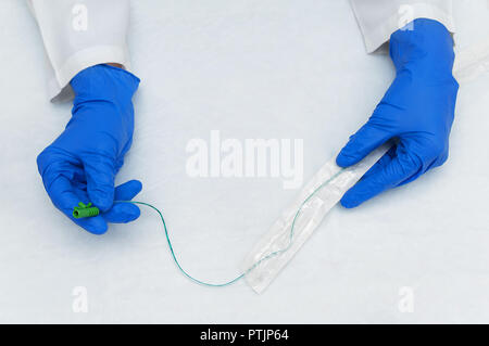 Die Hände eines Urologen in einem weißen Labormantel und Blau sterile Handschuhe nehmen sie einen Katheter aus einer sterilen Verpackung Stockfoto