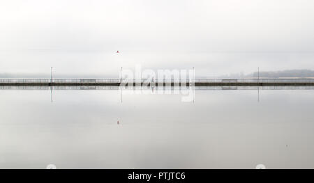 Einsamer Wanderer auf eine lange leere Brücke in den frühen Morgenstunden. Grau und neblig Wetter in der Stadt. Stockfoto