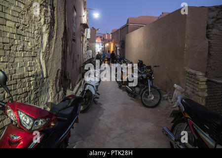 YAZD, IRAN - 10. AUGUST 2018: Motorcycyles in eine typische Straße der Altstadt von Yazd, Iran geparkt, in der Nacht mit seinen typischen Lehm Wände & Gebäude Stockfoto