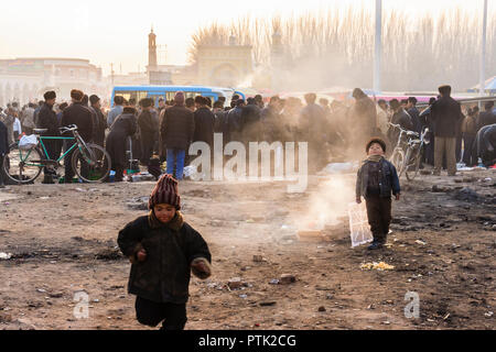 Kinder und Uyghar Männer in typischen Winter Kleidung sammeln bei Sonnenuntergang in einer Straße, der durch die Id kah-Moschee in der Altstadt von Kashgar, Xinjiang, China Stockfoto