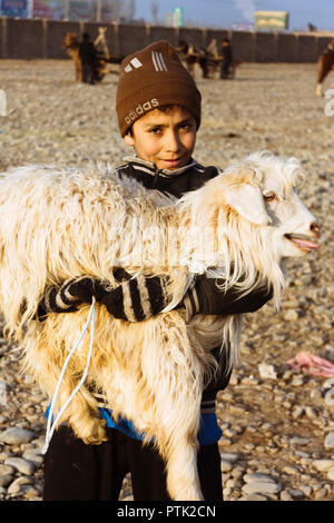 Kashgar, Xinjiang, China: Uiguren Junge hält ein Schaf in seine Arme bei Mal Basar, der grand Sonntag Viehmarkt von Kashgar. Stockfoto