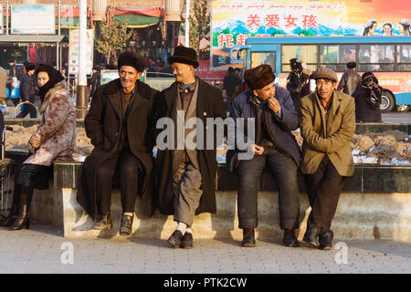 Kashgar, Xinjiang, China: Uiguren Männer sitzen und plaudern an der Straße in Kashgar. Stockfoto