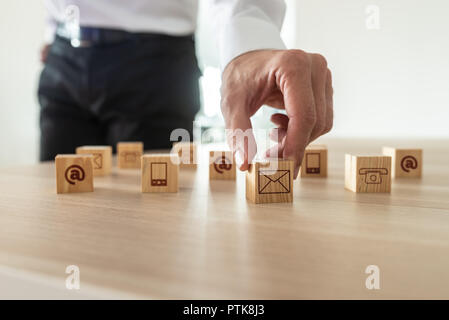 Kundenservice und Support Konzept - Geschäftsmann Inverkehrbringen Holzwürfel mit Kontakt und Kommunikation Symbole auf Sie auf Büro Schreibtisch. Stockfoto