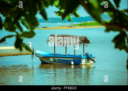 Kleine türkis Boot befindet sich in einem blauen Lagune vertäut. Malerische Szene gesehen, die durch die Bäume in Kalutara, Sri Lanka Stockfoto