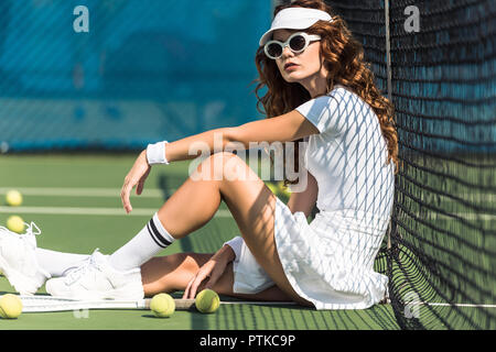 Seitenansicht des modischen weibliche Tennisspieler in Sonnenbrille in der Nähe von Netto auf Tennisplatz mit Geräten in der Nähe von Stockfoto