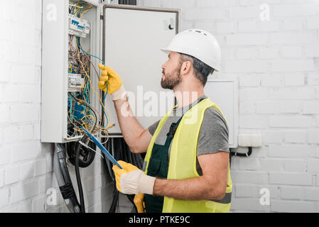 Seitenansicht der Elektriker holding Zwischenablage und prüfen Sie die Kabel im elektrischen Feld in Korridor Stockfoto