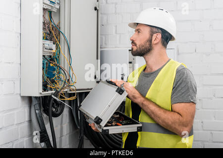 Seitenansicht des stattlichen Elektriker holding Toolbox und elektrische Feld im Korridor Stockfoto