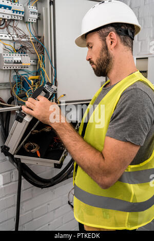 Seitenansicht des stattlichen Elektriker holding Toolbox in der Nähe von elektrischen Feld im Korridor Stockfoto