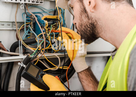 Seitenansicht der Elektriker Prüfen elektrischer Kasten mit multimetr im Korridor Stockfoto