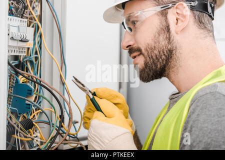 Seitenansicht des stattlichen Elektriker Zange halten und auf elektrische Feld im Korridor Stockfoto