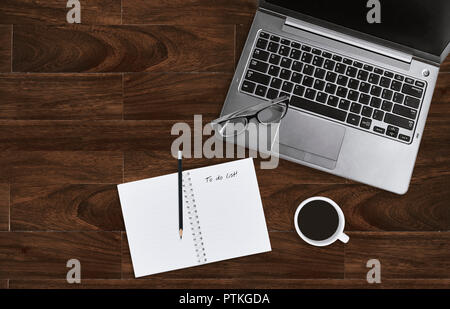 Laptop mit Brillen und öffnen Notebook mit leeren Seite der Aufgabenliste auf hölzernen Tisch Hintergrund mit kopieren. Business Office Schreibtisch Konzept. Nach oben V Stockfoto