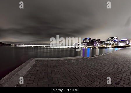 Niedrigen winkel Nacht Foto von Helsinki Salmisaari in der Nacht. Lange beleuchtete Brücke und bunten Bürogebäude auf dem Hintergrund einer schwarz-weißen Nacht Stockfoto