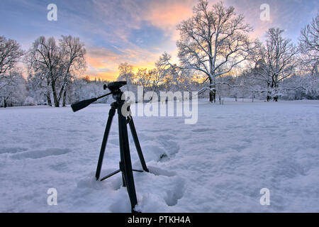 Hinter den Kulissen einer fotoshooting von Landschaft Fotograf. Erfassung von einem herrlichen Winter Sonnenuntergang in den verschneiten Wald. Stativ noch in der s Stockfoto