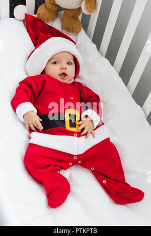 Hohe Betrachtungswinkel von adorable Baby in santa Anzug liegen in der Krippe mit Teddybär und Kamera Stockfoto