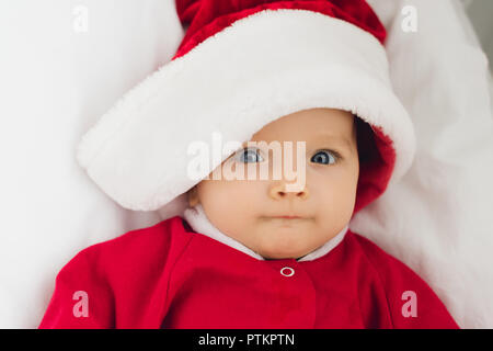 Close-up Portrait von entzückenden kleinen Baby in santa Anzug im Bett liegend und mit Blick auf die Kamera Stockfoto