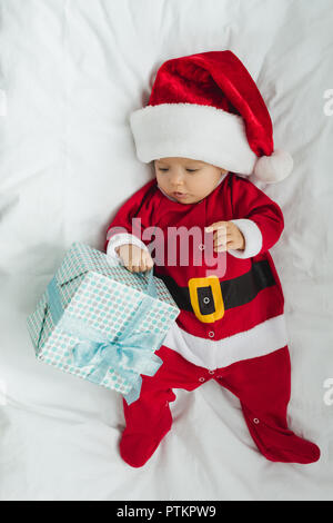 Blick von oben auf die entzückende kleine Baby in santa Klage in der Krippe liegend mit Weihnachtsgeschenk Stockfoto