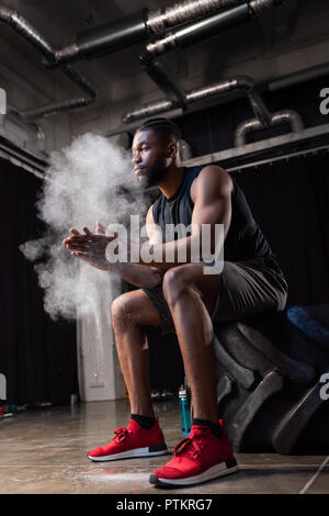 Low Angle View der afrikanischen amerikanischen Sportler sitzen in Reifen und mit Hilfe von Talkum auf die Hände Stockfoto