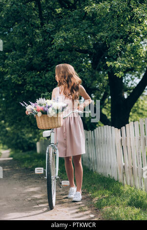 Junge Frau im Kleid mit retro Fahrrad mit Weidenkorb voller Blumen, Landschaft Stockfoto