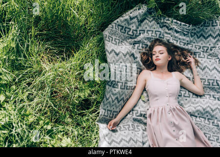 Ansicht von oben schöne nachdenkliche Frau in Kleid liegen auf Leere auf grünem Gras in Park Stockfoto