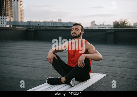 Stattliche Sportsman stretching Beine auf Yoga Matte auf dem Dach Stockfoto