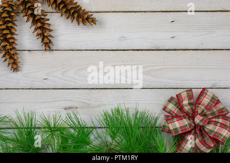 Eine untere Grenze von white pine Ästen und einer roten und grünen Bogen mit drei weißen Tannenzapfen in der linken oberen Ecke Stockfoto