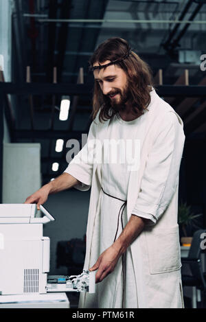 Happy Jesus in Dornenkrone und Robe mit Copy Machine in modernen Büro Stockfoto