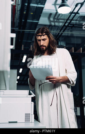 Konzentrierte sich Jesu in Dornenkrone und robe Kontrolle Papiere in der Nähe Kopierer in modernen Büro Stockfoto