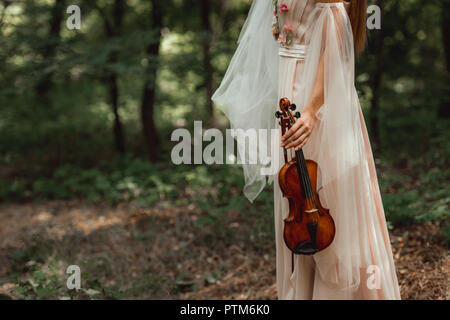 7/8-Ansicht von Mädchen im Kleid mit Blumen holding Violine in Wäldern Stockfoto