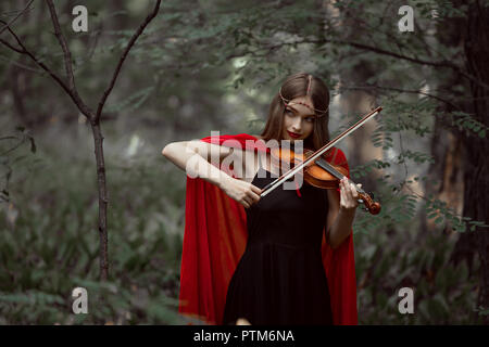 Attraktive mystic Mädchen im roten Mantel das Spielen auf Violine im Wald Stockfoto