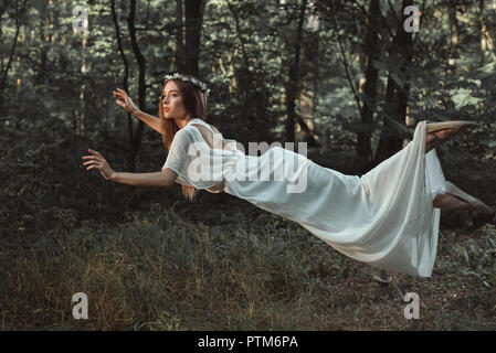 Elegante schöne Mädchen in weißem Kleid im Wald fliegen Stockfoto