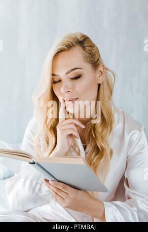 Junge blonde Frau im Pyjama Buch in Schlafzimmer konzentriert Stockfoto