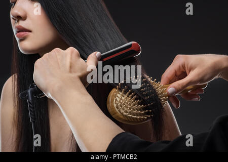 Teilweise mit Blick auf die Friseur glätten womans Haar mit einem Glätteisen und Bürste isoliert auf Schwarz Stockfoto