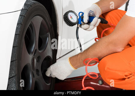 Zugeschnittenes Bild der Automechaniker Aufpumpen von Reifen und Luft mit Manometer prüfen. Stockfoto