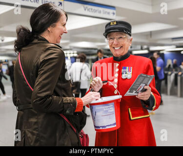 Victoria Station, London, 10. Okt 2018. Eine weibliche Chelsea Rentner in der traditionellen scharlachroten Mantel nimmt eine Spende in Victoria Station. Die Veteranen sammeln Spenden in zwölf Londoner U-Bahn-Stationen, heute im Namen der Nächstenliebe "erinnert". Eröffnungs-Projekt der Nächstenliebe", es aber nicht Es' hat das Ziel, zum Gedenken an jene, die in der WK 1 starb, die Jungen zu erziehen und die heutigen Veteranen leiden von der mentalen und körperlichen Wunden der Service während der Hundertjahrfeier 2018 heilen. Credit: Imageplotter Nachrichten und Sport/Alamy leben Nachrichten Stockfoto