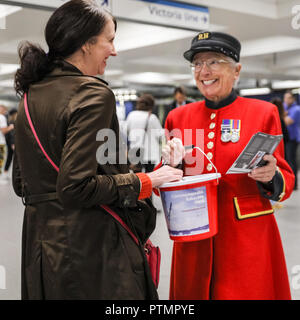 Victoria Station, London, 10. Okt 2018. Eine weibliche Chelsea Rentner in der traditionellen scharlachroten Mantel nimmt eine Spende in Victoria Station. Die Veteranen sammeln Spenden in zwölf Londoner U-Bahn-Stationen, heute im Namen der Nächstenliebe "erinnert". Eröffnungs-Projekt der Nächstenliebe", es aber nicht Es' hat das Ziel, zum Gedenken an jene, die in der WK 1 starb, die Jungen zu erziehen und die heutigen Veteranen leiden von der mentalen und körperlichen Wunden der Service während der Hundertjahrfeier 2018 heilen. Credit: Imageplotter Nachrichten und Sport/Alamy leben Nachrichten Stockfoto